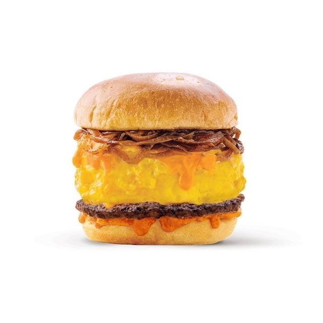 A burger with a beef patty, melted cheddar cheese, caramelized onions, and an orange sauce, sandwiched between a soft, lightly toasted bun. The cheese is flowing over the sides, and the ingredients appear fresh and appetizing. The background is plain white.